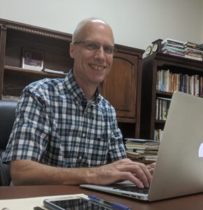 Paul Schrag sitting at his desk typing on his laptop.