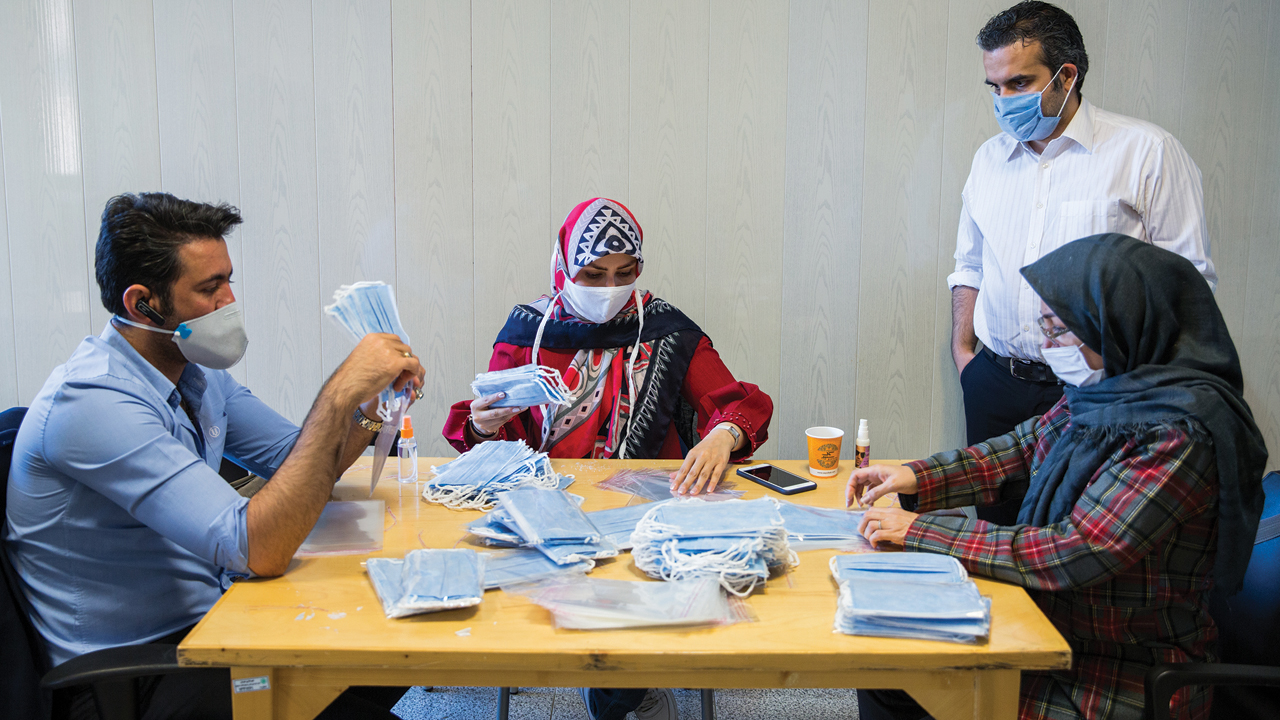 Ashkan Taghipour, standing, director of the Moms Against Poverty partner non­governmental organization in Tehran, Iran, supervises staff and volunteers repackaging masks sent by Mennonites. — Doug Hostetter