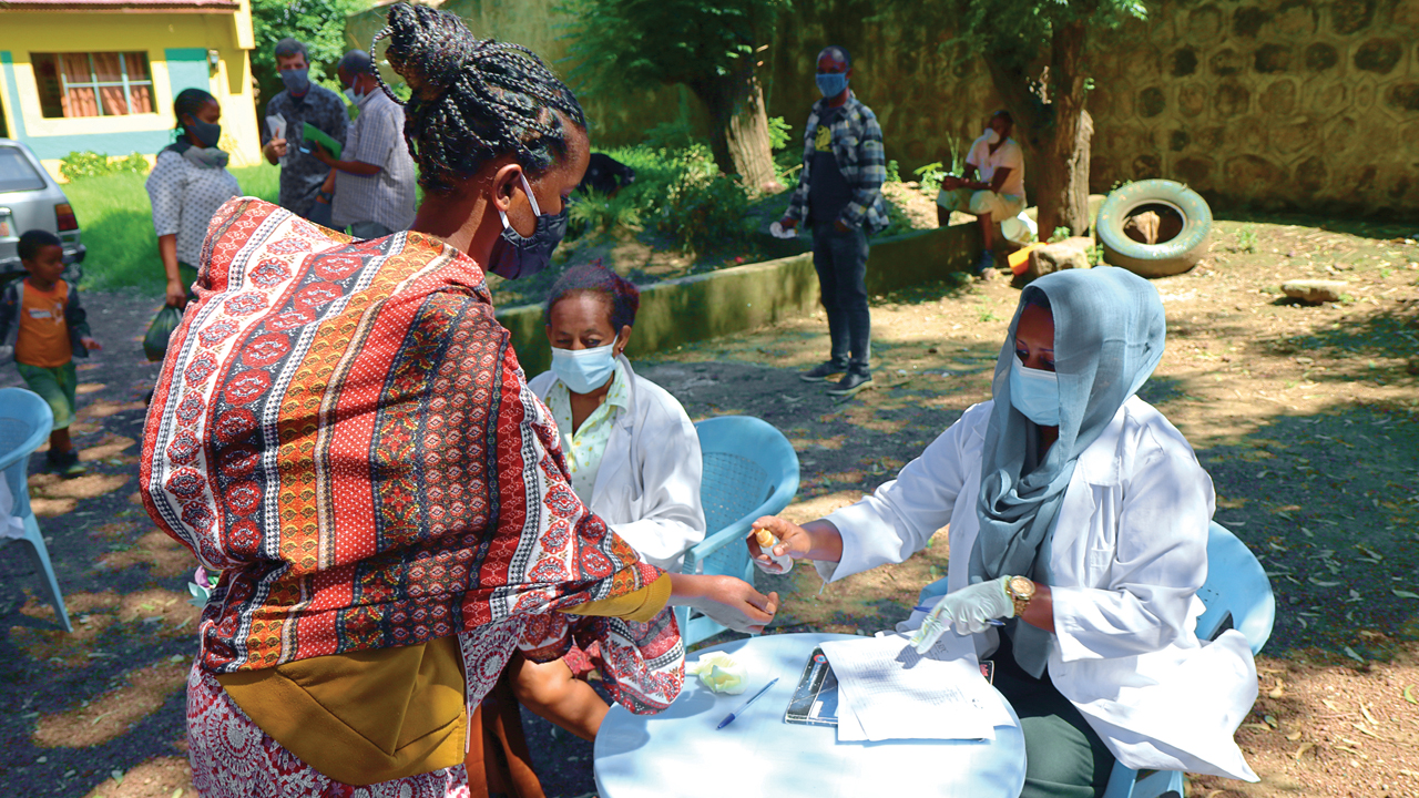 Head teacher Madina Abrahim sprays sanitizer on the hands of Bayish Tababain in early September before she signs in to collect food and soap at Meserete Kristos Church preschool in Adama, Ethiopia. The four-month, MCC-supported project is intended to help combat rising food prices and unemployment caused by the coronavirus pandemic. — Rose Shenk/MCC