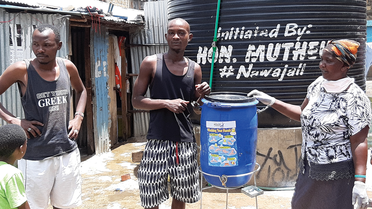 Rosneka Mulalyah, right, promoter for the Centre for Peace and Nationhood, presents a handwashing station to Paul Karuiki and Mike Musyoki in Nairobi, Kenya. Mennonites in Nairobi are helping prevent the spread of COVID-19 by installing handwashing stations. — Mennonite World Conference