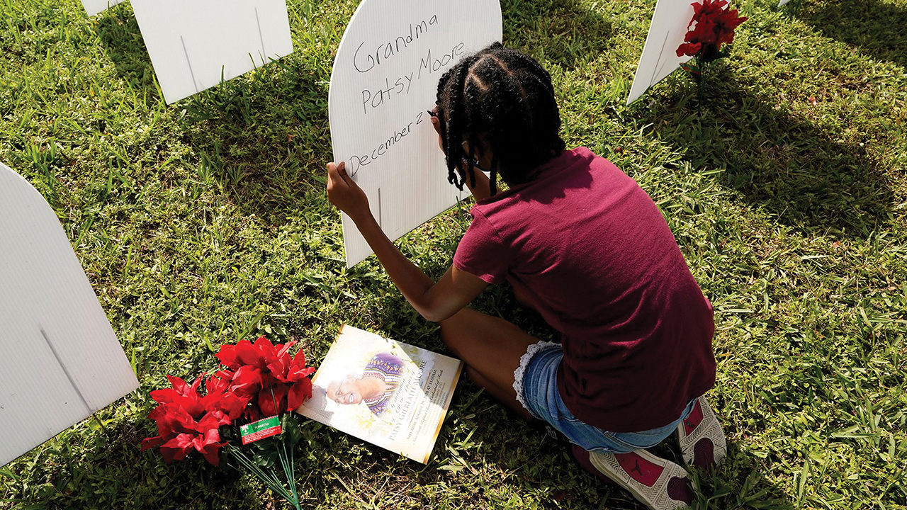 On Nov. 24, Kyla Harris, 10, writes a tribute to her grandmother Patsy Gilreath Moore, who died at age 79 of COVID-19, at a symbolic cemetery created to remember and honor lives lost to COVID-19 in the Liberty City neighborhood of Miami. — Lynne Sladky/AP