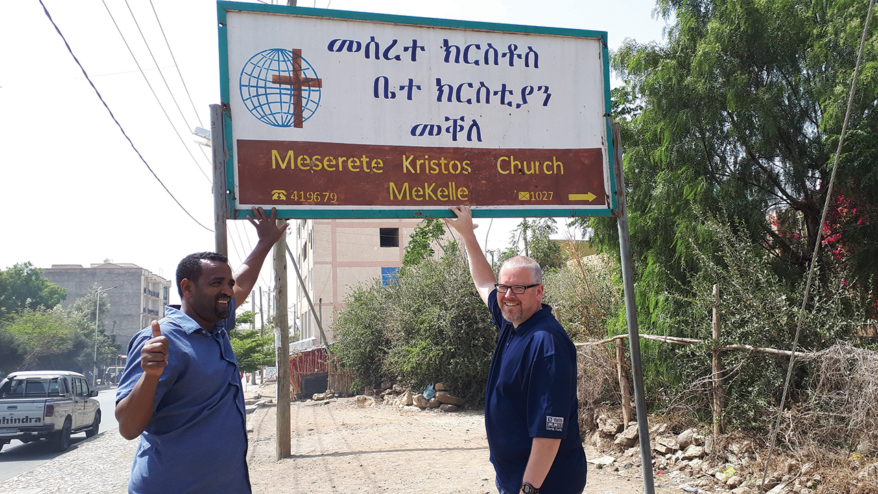 Fanosie Legesse, Mennonite Church Eastern Canada intercultural mission minister, left, and MCEC mission minister Norm Dyck stand in 2019 at the sign for the Meserete Kristos Church congregation in Mekelle, capital of the Tigray region of Ethiopia, which is at the center of the current conflict. — Mennonite Church Canada
