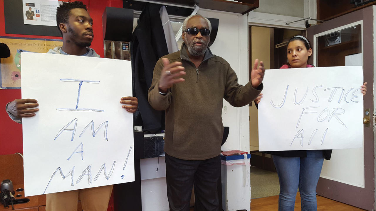 Stan Maclin, with then-undergraduate Eastern Mennonite University students Phillip Watson and Amanda May, speaking about the civil rights movement in Tyrone Sprague’s barbershop in downtown Harrisonburg, Va., on Martin Luther King Jr. Day in 2016. — Celeste Thomas