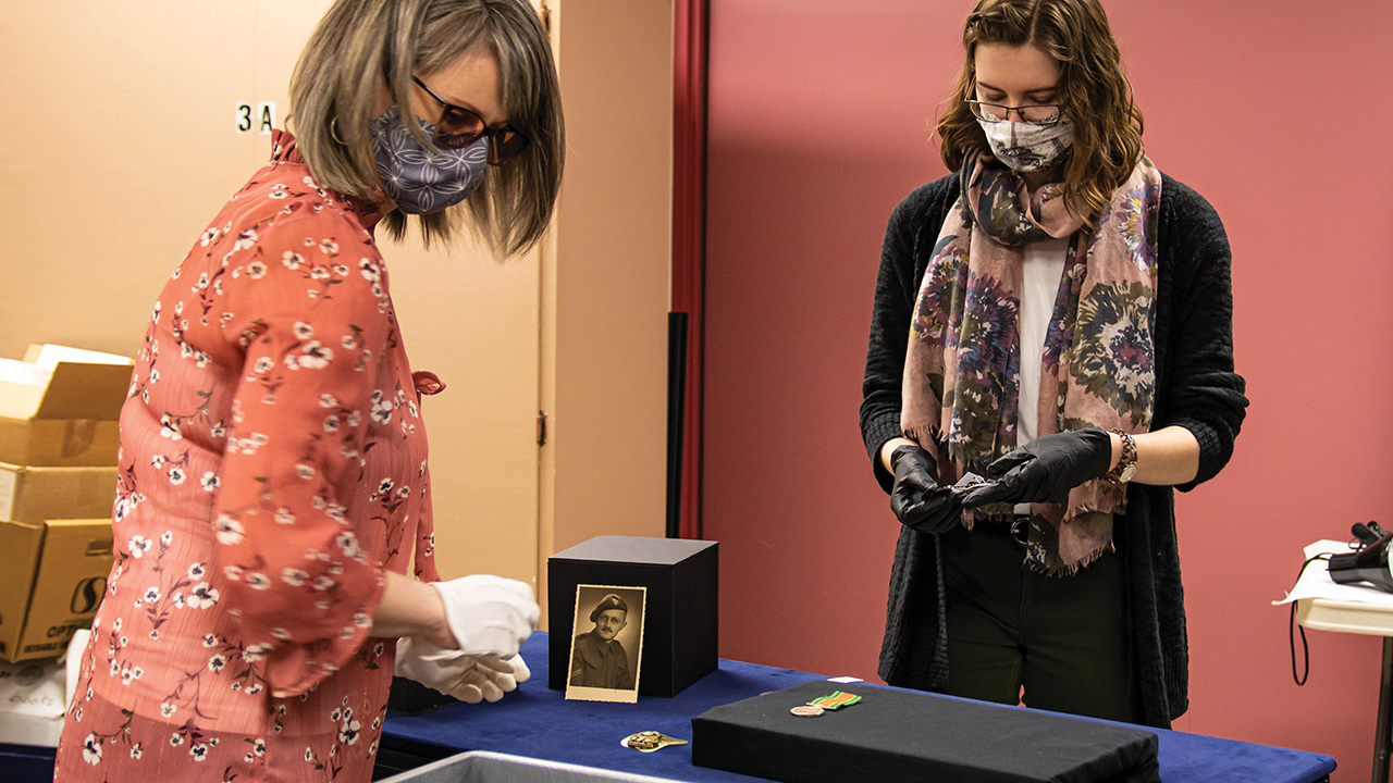 Mennonite Heritage Village senior curator Andrea Klassen, left, and curatorial assistant Kara Suderman work on a display case featuring some of the artifacts that will be part of the “Mennonites at War” exhibit. — Mennonite Heritage Village