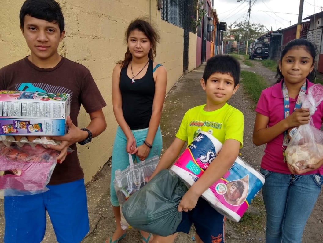 Grupo de niños de Guarari, Heredia Costa Rica recibiendo paquetes alimenticios de la Iglesias Menonita Discípulos de Jesús. Ashley, Anayanci, Sebastián, Geovani. Foto de Cindy Alpizar.