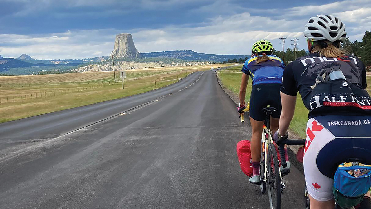 Cyclists Joanna Friesen and Miriam Huebner approach Mato Tipila — “Bear Lodge” in Lakota, also known as Devils Tower — in northeastern Wyoming on the Center for Sustainable Climate Solutions cross-country ride. — Sierra Ross Richer