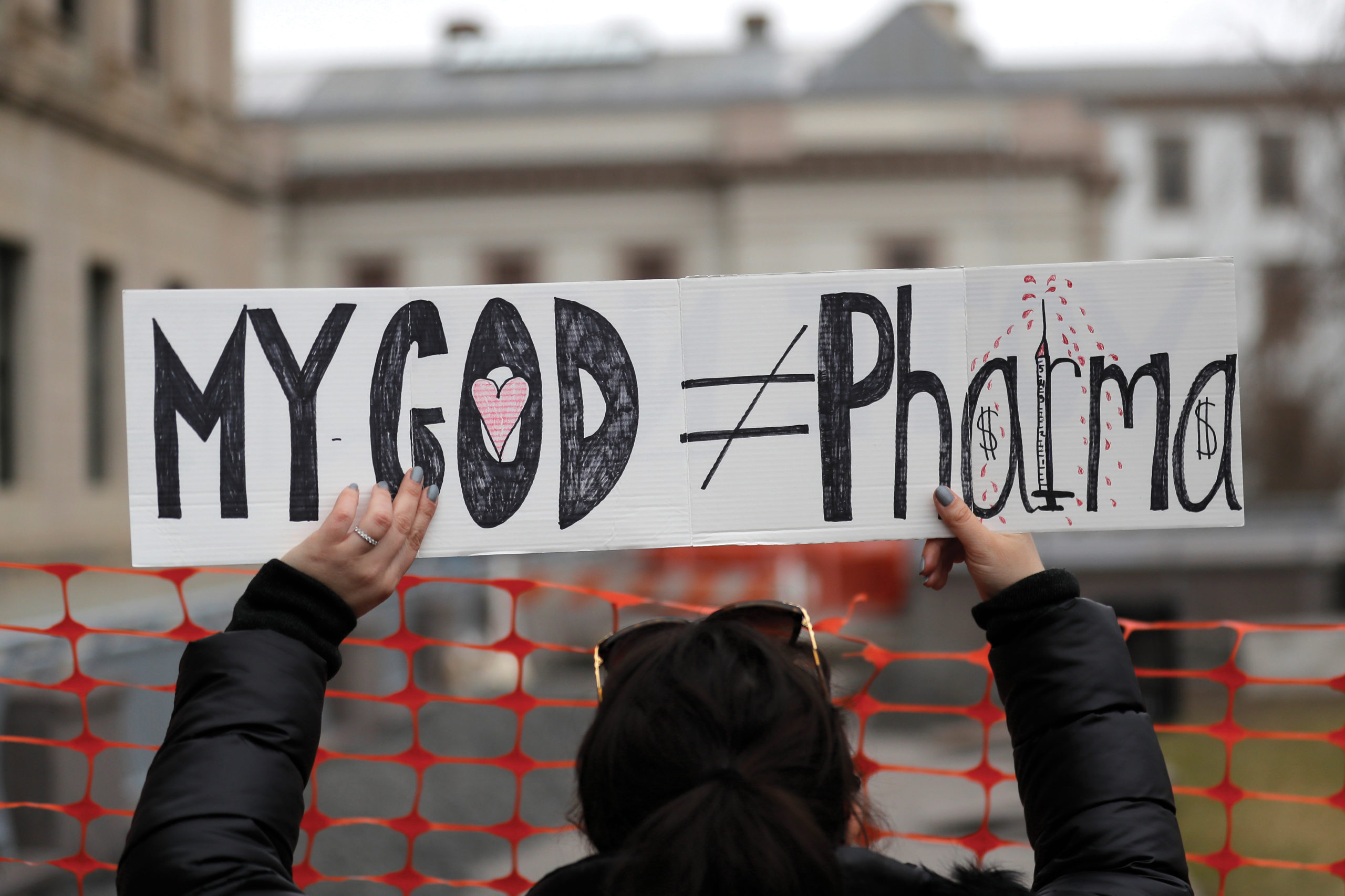On Jan. 13, 2020, a woman holds a sign during a protest at the state house in Trenton, N.J. Religious objections, once used only sparingly to get exempted from required vaccines, are becoming a widely used loophole against the COVID-19 shot. — Seth Wenig/AP