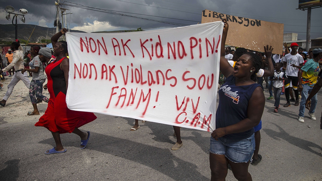 People protest Oct. 19 carrying a banner with a message that reads in Creole: "No to kidnappings, no to violence against women! Long live Christian Aid Ministries," demanding the release of kidnapped missionaries, in Titanyen, north of Port-au-Prince, Haiti. A group of 17 U.S. mission workers including five children, was kidnapped Oct. 16 by a gang in Haiti. (Joseph Odelyn/AP)