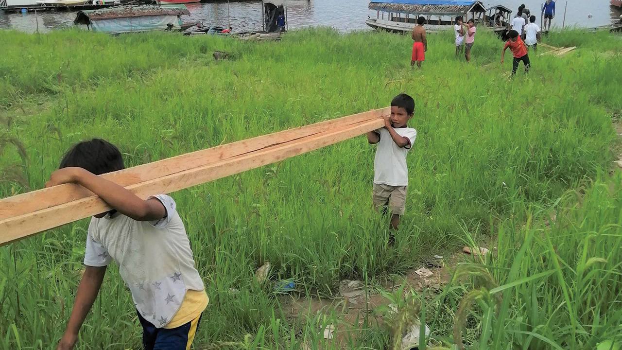 Children carry wood from a boat to the building site for the houses. — David Moreno