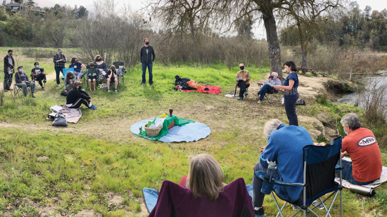 Worshipers at Wild Church in Fresno, Calif., gather around communion elements by a river. — Mennonite Church USA