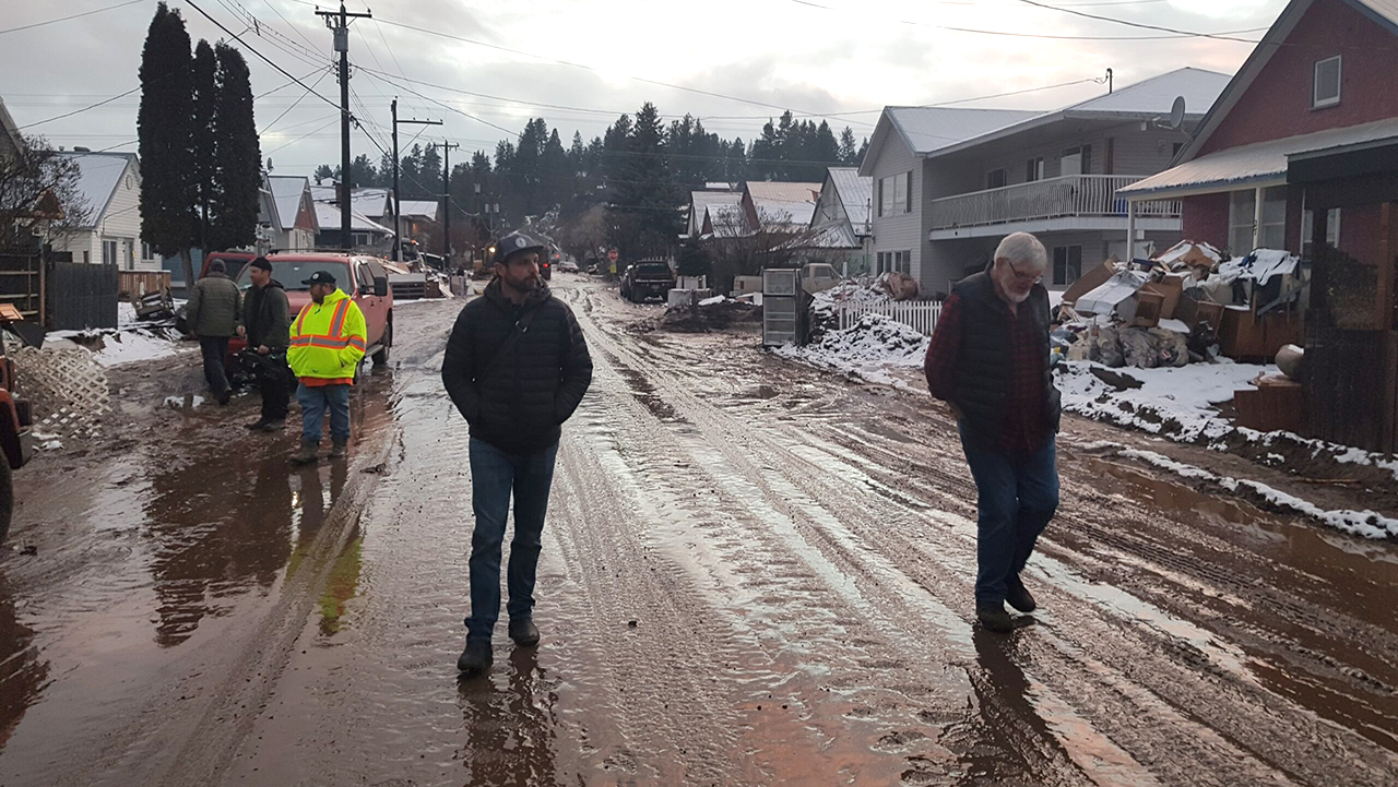 Walter Wiebe, right, walks with Kyle Nichols, left, along a muddy formerly flooded street last year in Princeton, B.C. — Mennonite Disaster Service