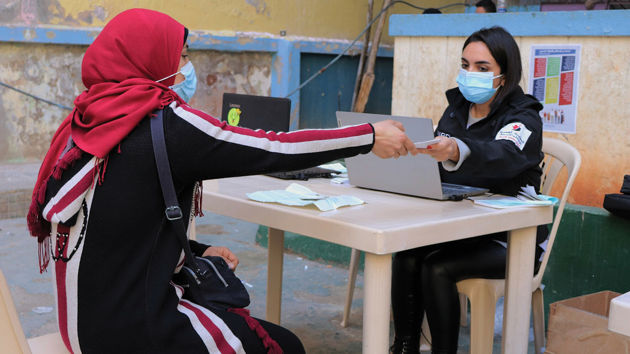 Aziza Samir Al Lahham of Beirut, Lebanon, receives a food voucher from a staff member of Popular Aid for Relief and Development, a Mennonite Central Committee partner. — Popular Aid for Relief and Development