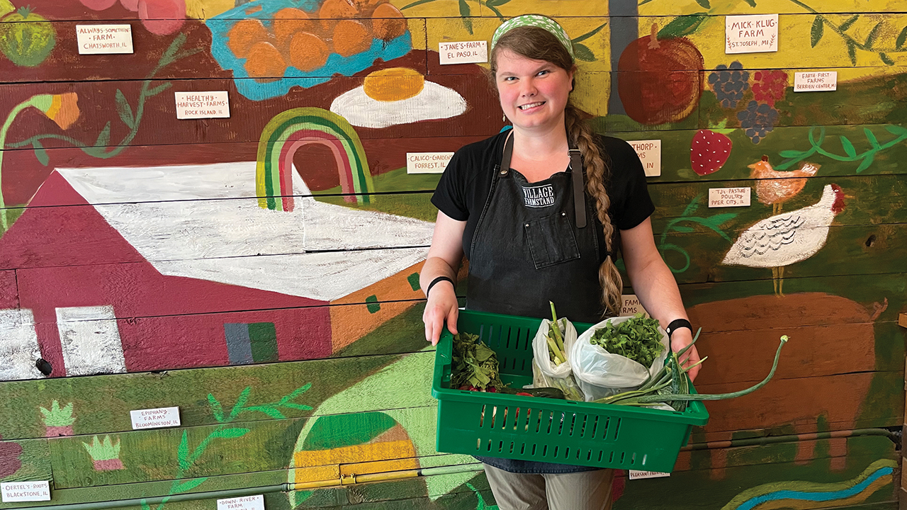 Cassidhe Hart holds pick bin items in front of a hand-painted mural inside the Village Farmstand store in Evanston, Ill. — Bonnie Nield