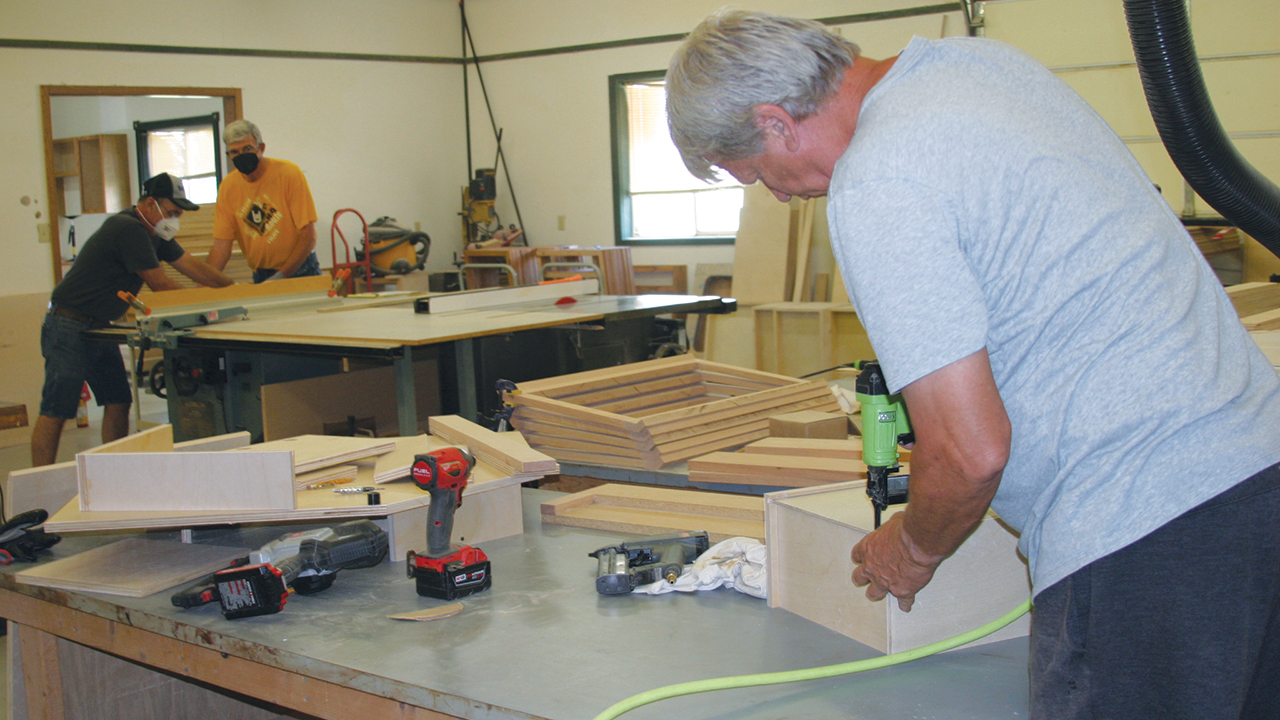 Steve Voth, right, assembles cabinets July 6 at a new Mennonite Disaster Service shop in Goessel, Kan., while Rod Abrams, left, and Delbert Peters cut components on a table saw. — Tim Huber/AW