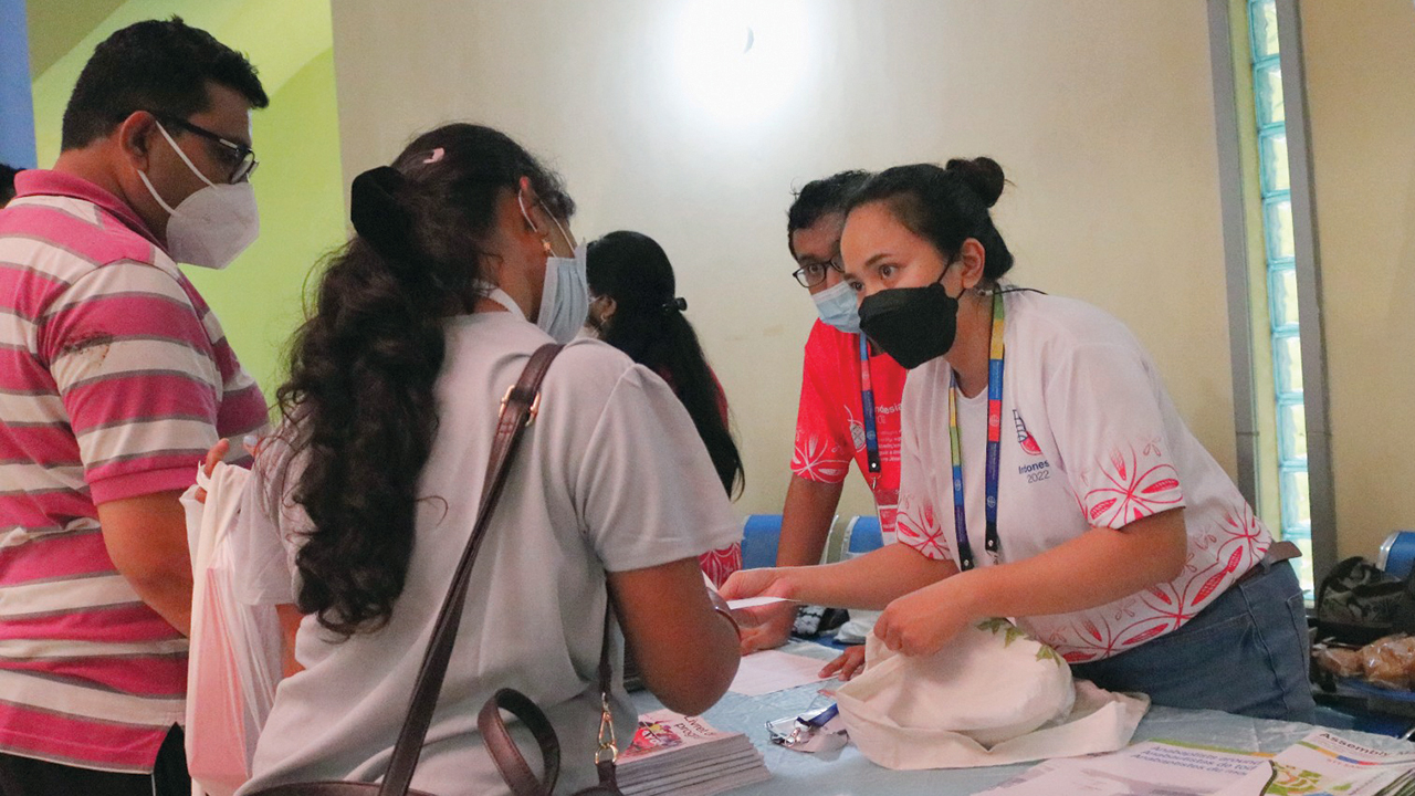Rut Arsari, center, helps Mennonite World Conference Assembly participants at the registration table. — Loyce Twongirwe/MWC