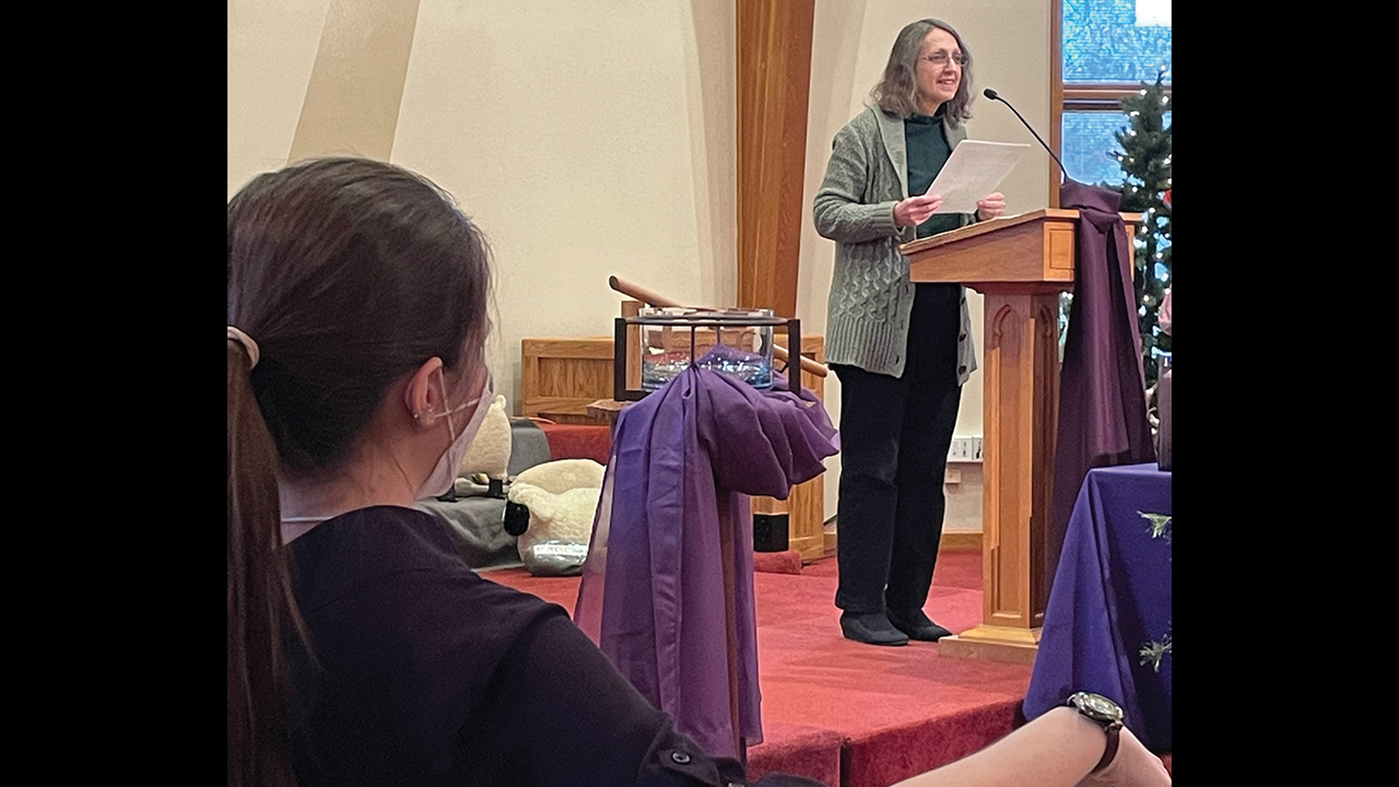 Shari Wagner reads the sermon Dec. 11 at First Mennonite Church in Indianapolis while Pastor Monica Miller observes. — Cara Yoder