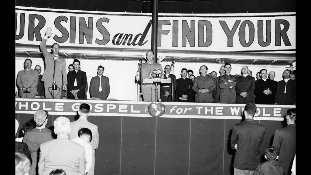 George R. Brunk II stands at the pulpit as his brother, Lawrence, left, leads singing during a Brunk Brothers’ Revival Campaign event. — Menno Simons Historical Library