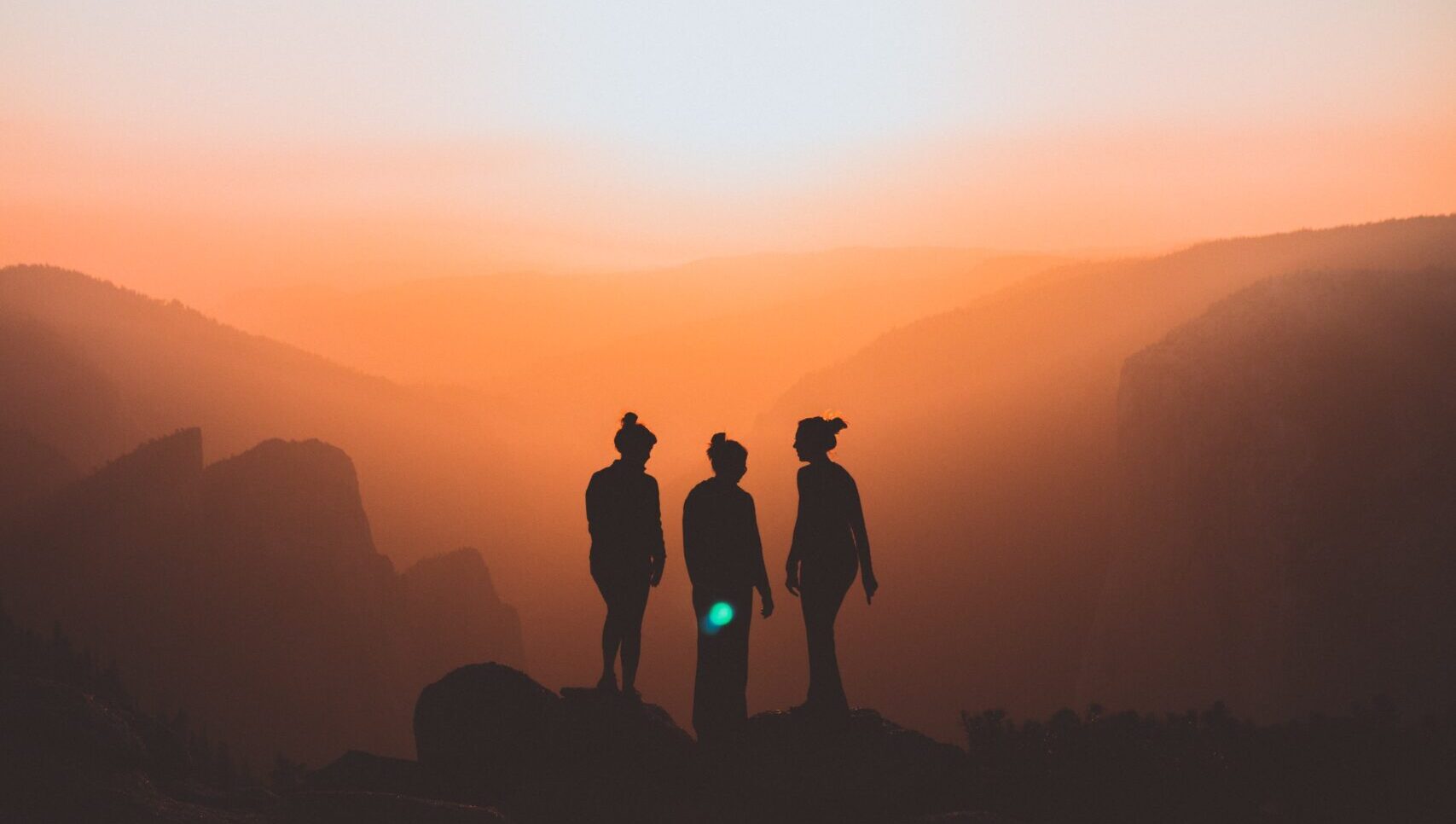 Three women's silhouettes standing on an elevated hill.