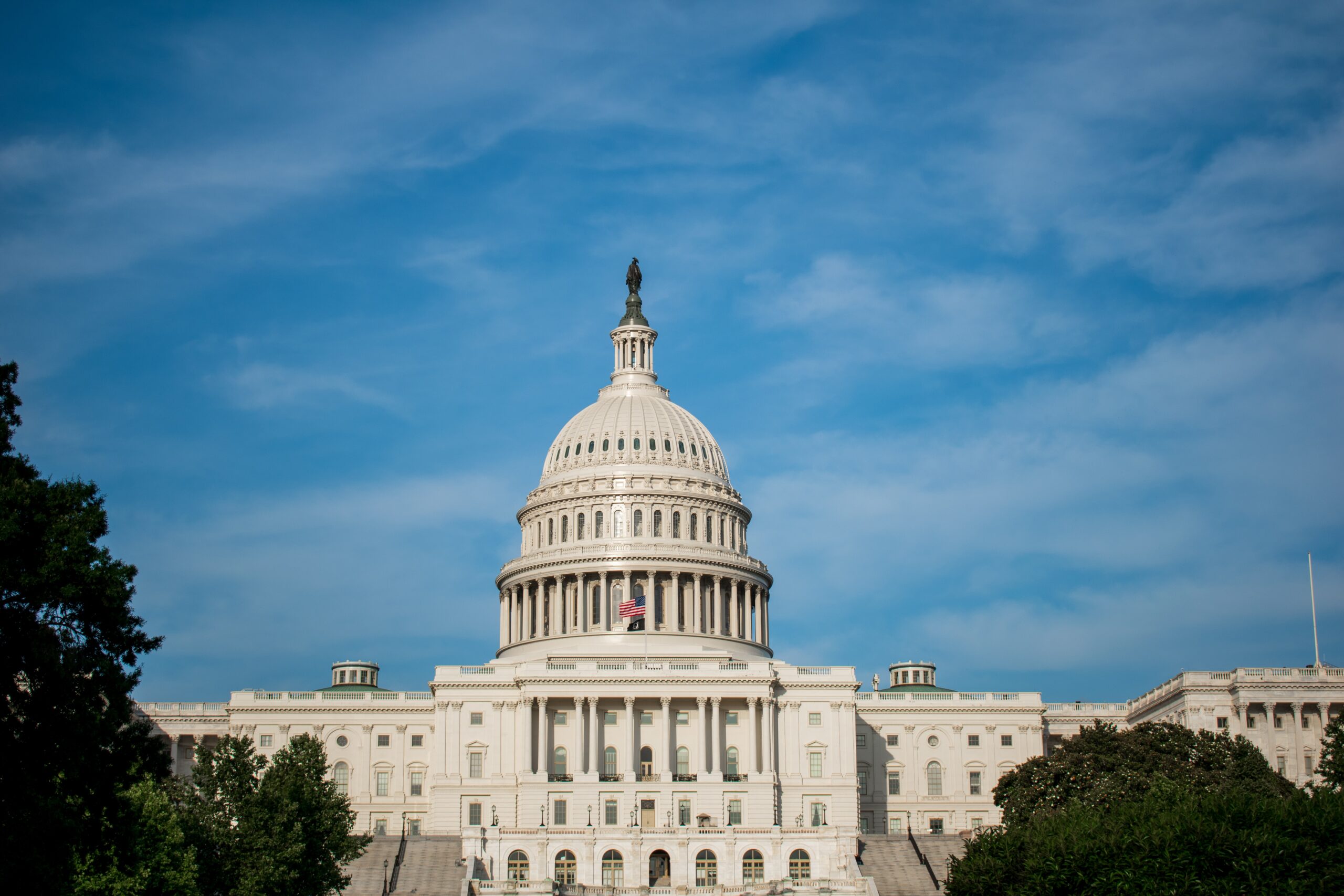 The white US Capitol building in front of a blue sky with some clouds.