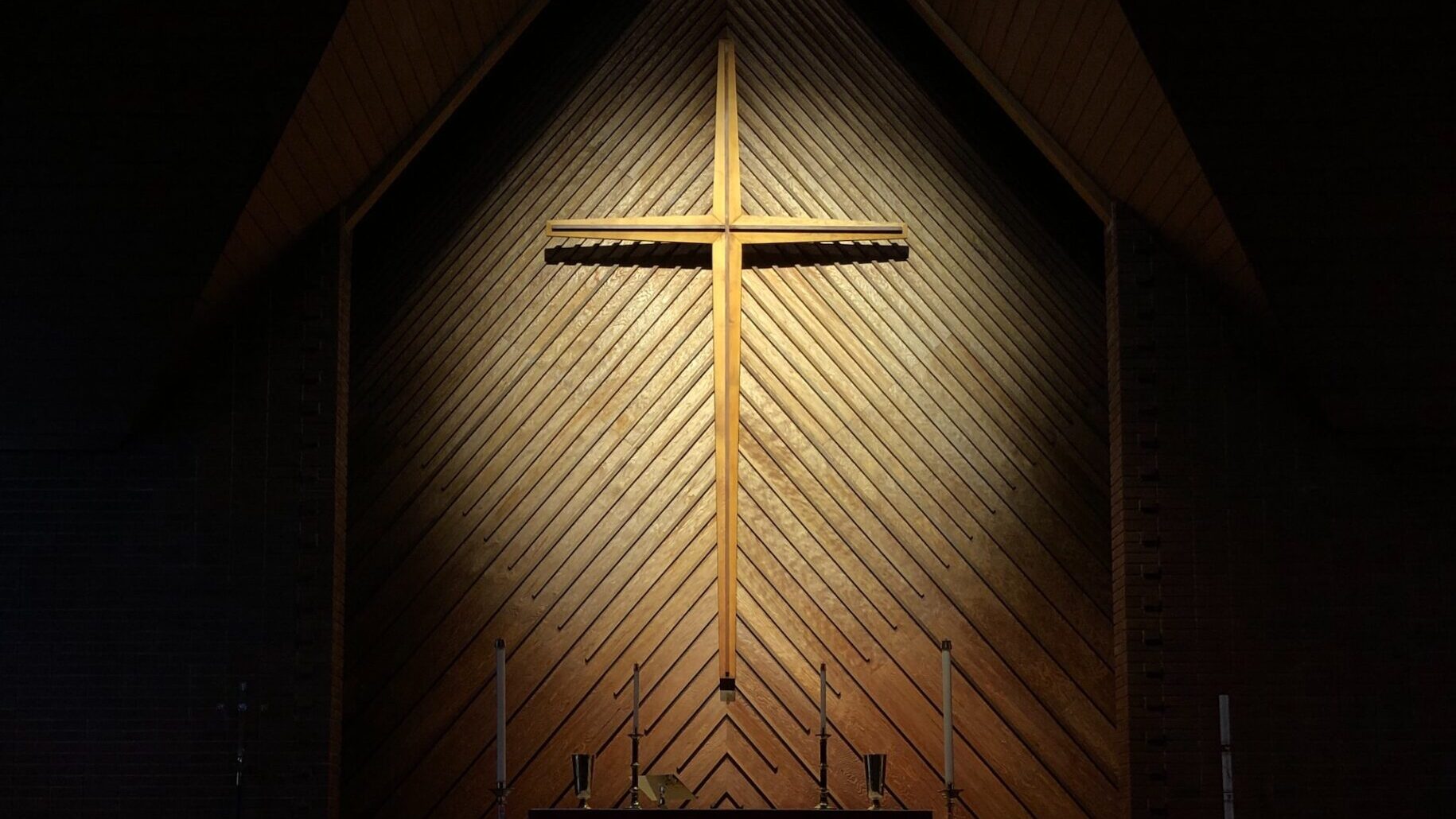 Wooden cross in a spotlight surrounded by darkeness.