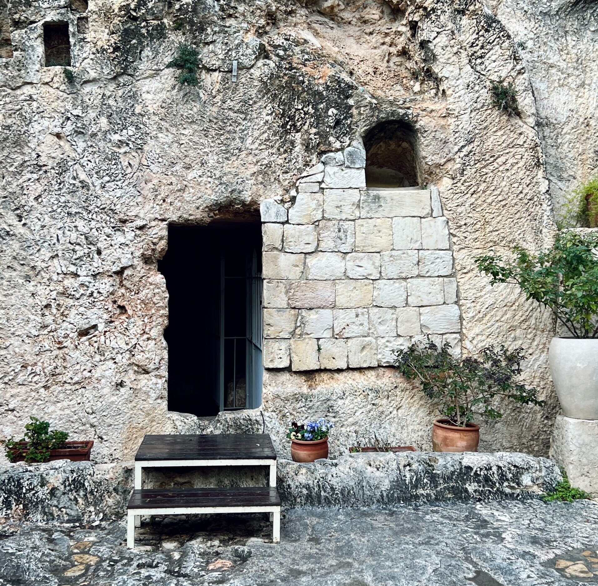 Gray tomb with open door and green plants in pots near the door.