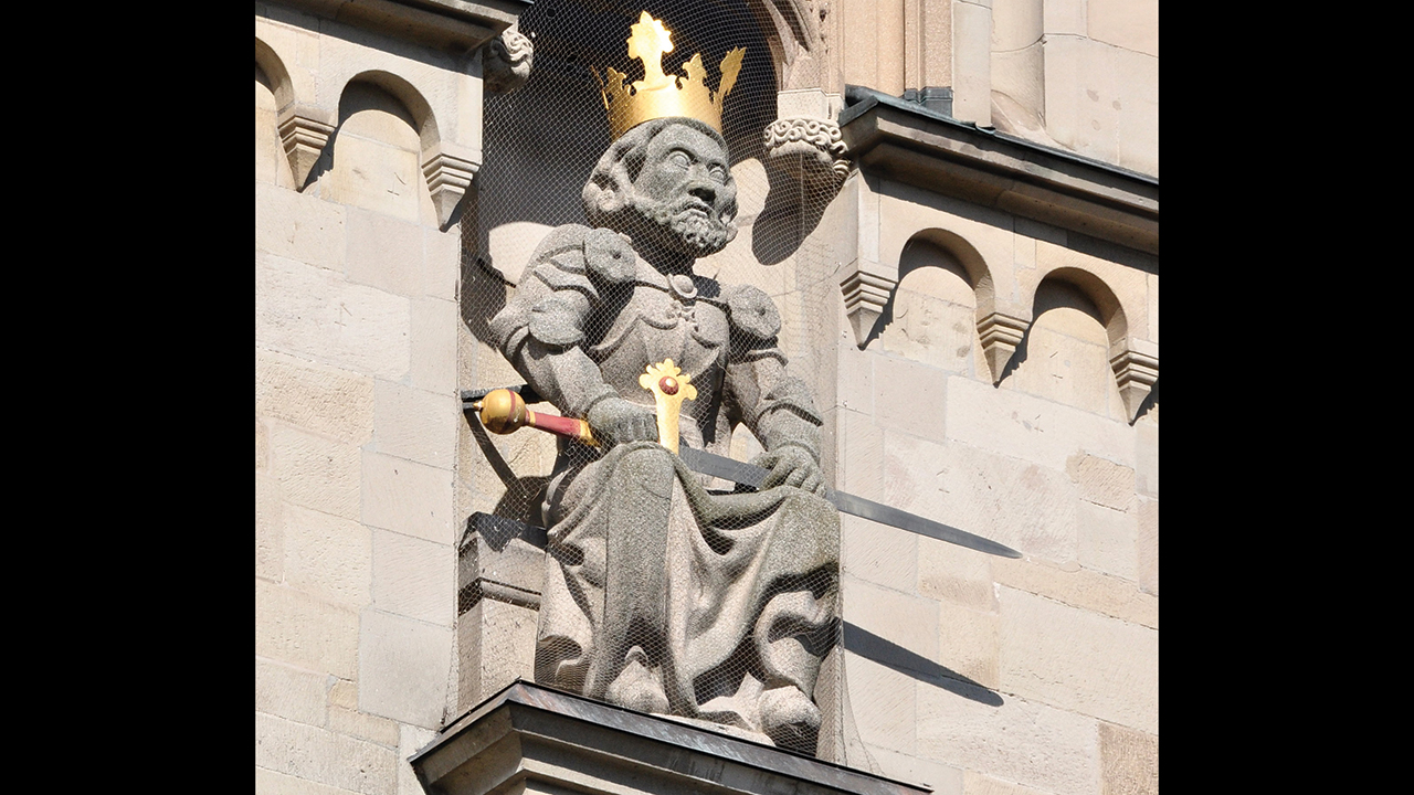 A statue of the Holy Roman Emperor Charlemagne on the south tower of the Grossmünster cathedral in Zurich, Switzerland, holds a sword and scepter symbolizing the military and civil authority that suppressed the Anabaptist movement, which began in Zurich. — Roland zh/Wikimedia Commons