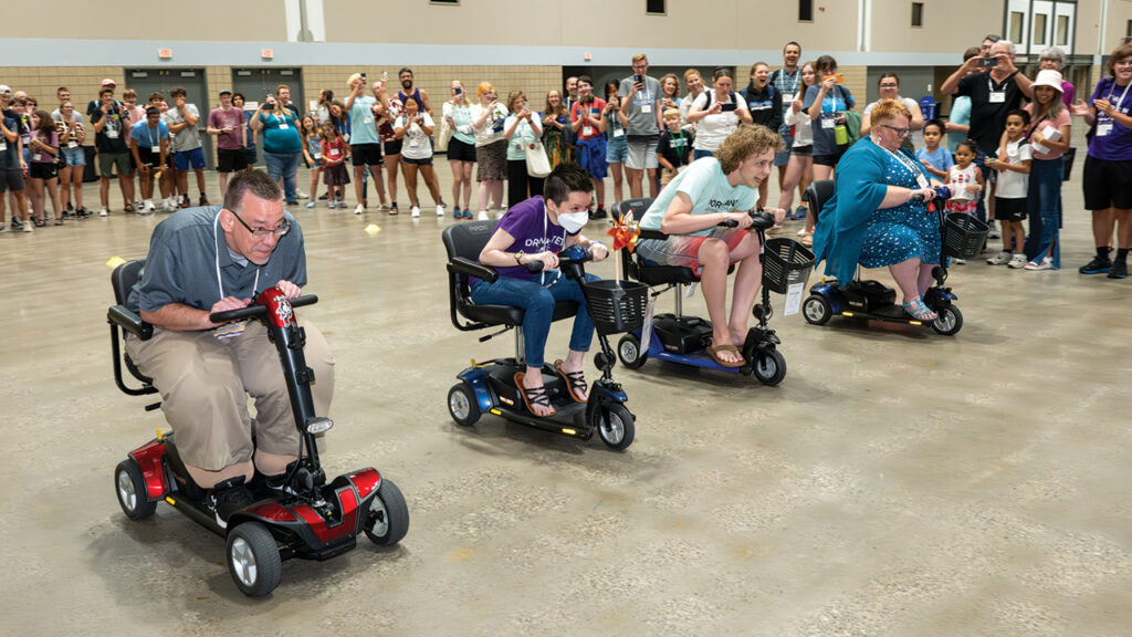 Mark Woods of Dalton, Ohio, Monica Miller of Indianapolis, Izak Lutz of Portland, Ore., and Angela Studebaker of Goshen, Ind., compete in a mobility scooter race in the recreation hall. Scooters were provided to increase accessibility in the vast convention center. — Ken Krehbiel/MC USA