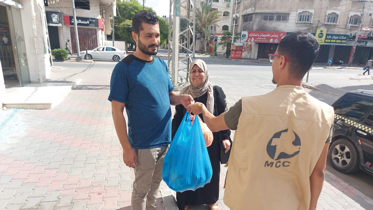Al-Najd Developmental Forum volunteer Firas Hamlawi, right, and staff member Rifqah Hamlawi, center distribute food packages and bedding Oct. 17 to families displaced by the current violence in the Gaza Strip. The recipient is not named for security purposes. Al Najd is a Mennonite Central Committee partner. — Al-Najd Developmental Forum
