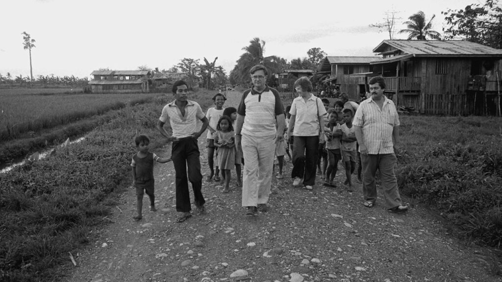 John A. Lapp, center, and wife Alice Lapp, and Mennonite Central Committee Indonesia staff Allen Harder, right, walk with residents of Agusan Village in northeastern Mindanao, Philippines. The Lapps joined Asia service workers at a regional retreat in 1986. — Earl Martin/MCC