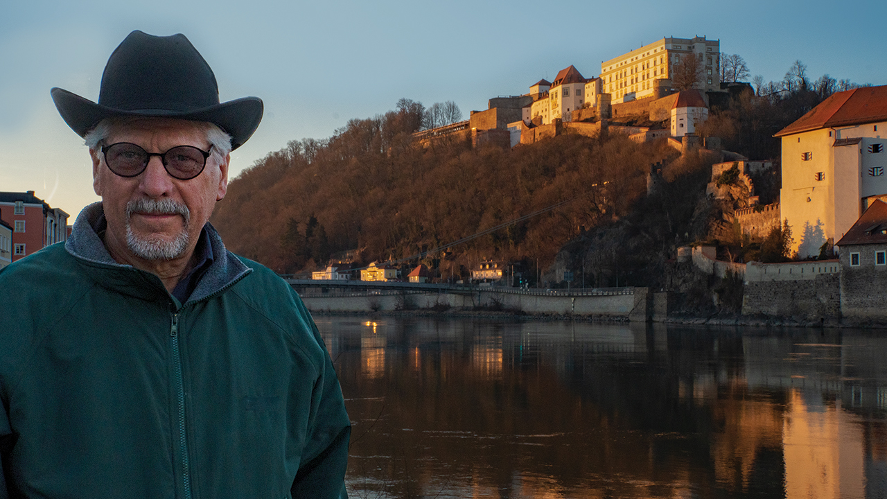 Elam Stoltzfus by the Danube River in Passau, Germany, with the Oberhaus castle, where Anabaptist prisoners wrote Ausbund hymns, in the background. — Nic Stoltzfus