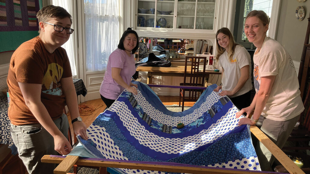2022-23 MVS San Francisco unit participants Eli Reimer, Claire Waidelich (2020-2022 participant), Rachel Miller and Anna Lubbers work on a quilt together at the unit house. — Mennonite Mission Network