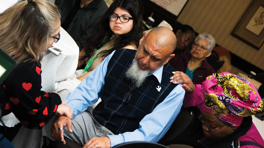 Participants lay hands over Gilbert Hernandez of San Antonio Mennonite Church and Western District Conference. — Juan Moya/AW