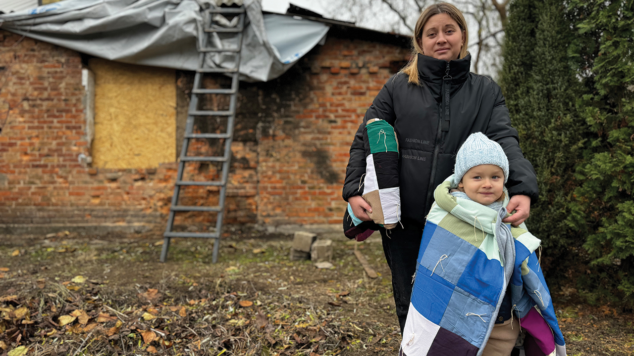 Yana and her daughter, who live in Nikopol, Ukraine, stand in front of their damaged home, with comforters from Mennonite Central Committee. Shelling from Russian military forces has partially destroyed their home, leaving it unsafe to stay in. —New Life Charitable Fund