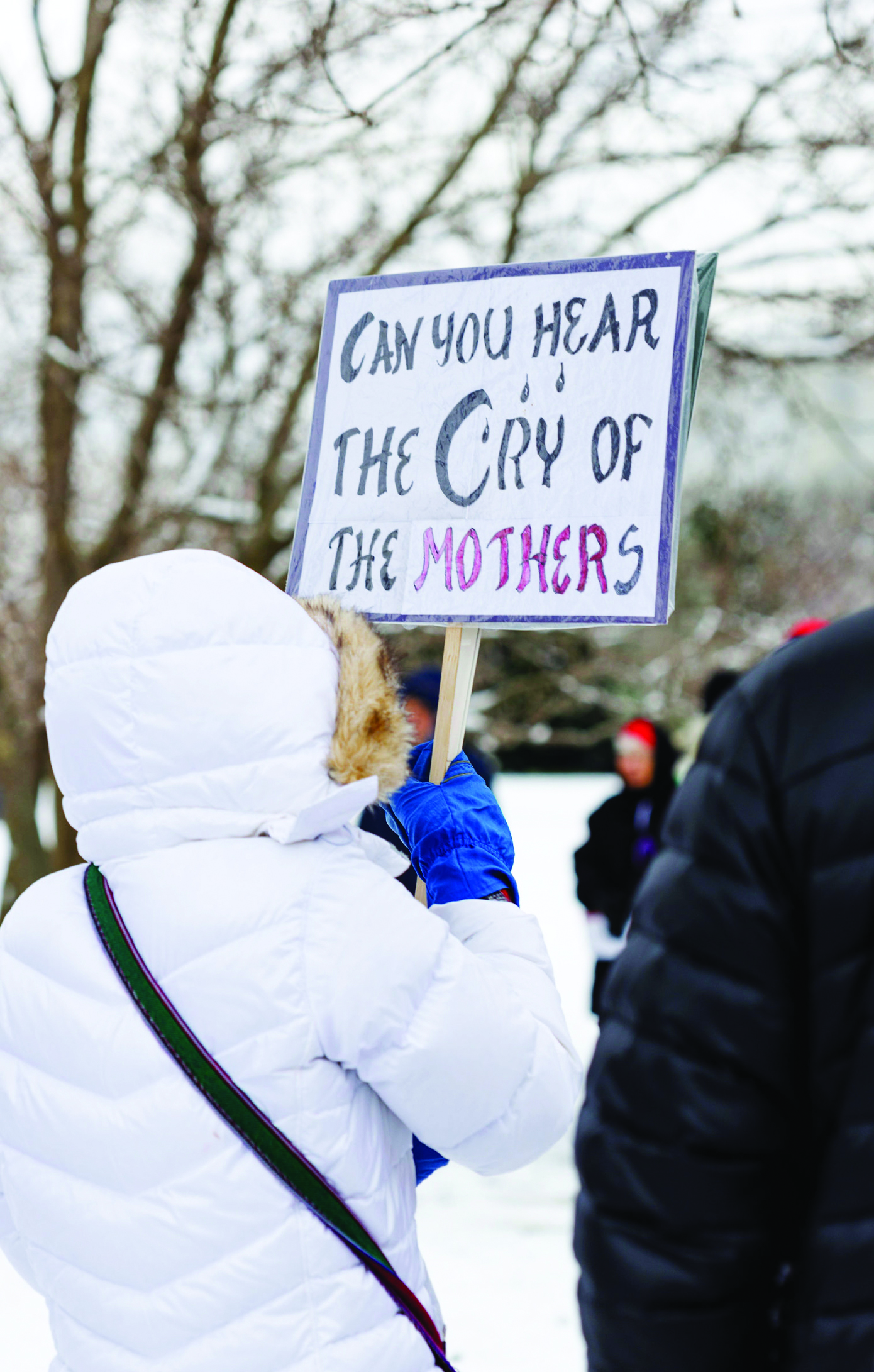 An individual holds a sign that reads cry of mothers from Mennonite Action.