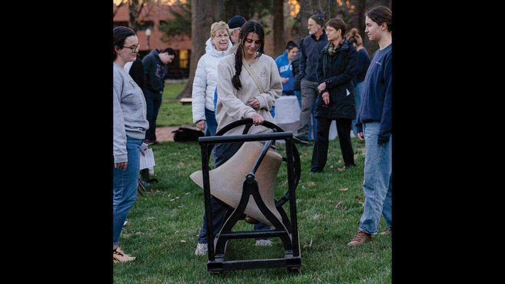 Maddison Terrell rings a bell on the Bethel College campus to mourn live lost in Gaza and Israel as Harley McCormick, left, and Abigail Chappell Deckert, right look on. — Andrew Graber
