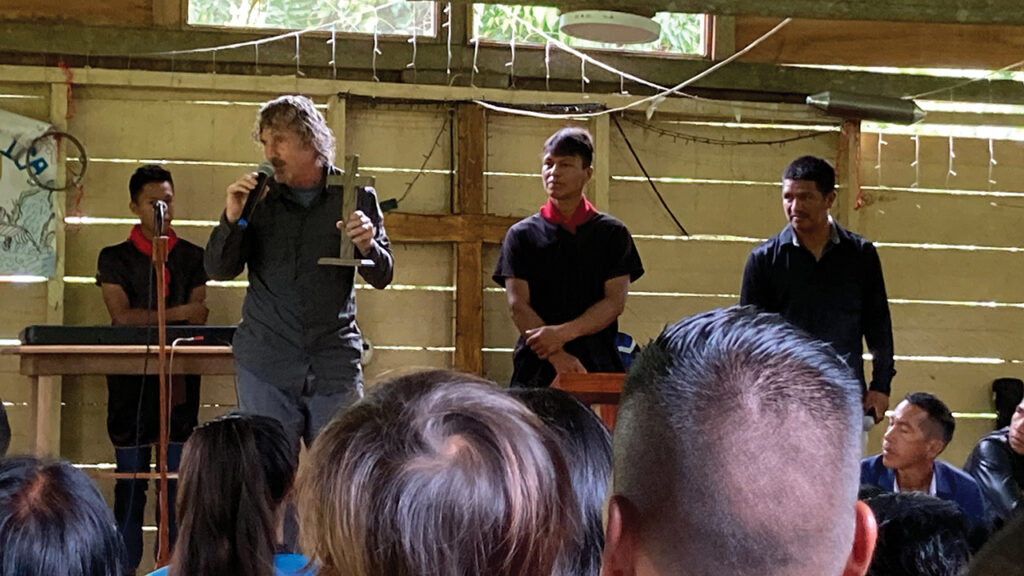 Jerrell Ross Richer presents a gift from his home congregation, Waterford Mennonite Church in Goshen, Ind., to Living Water Evangelical Church. The wooden cross was handmade by Waterford member Luke Voth. In the center is Hiter Yiyoguaje, with his brother Carlos, right, and son Charles, left. — Jane Ross Richer/MMN