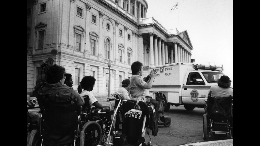 With a raised fist, Eleanor Smith cheers an arrested cohort ejected from the U.S. Capitol in an action to spur the Americans with Disabilities Act in 1990. — Used by permission. © Tom Olin Collection, MSS-294. Ward M. Canaday Center for Special Collections, The University of Toledo Libraries