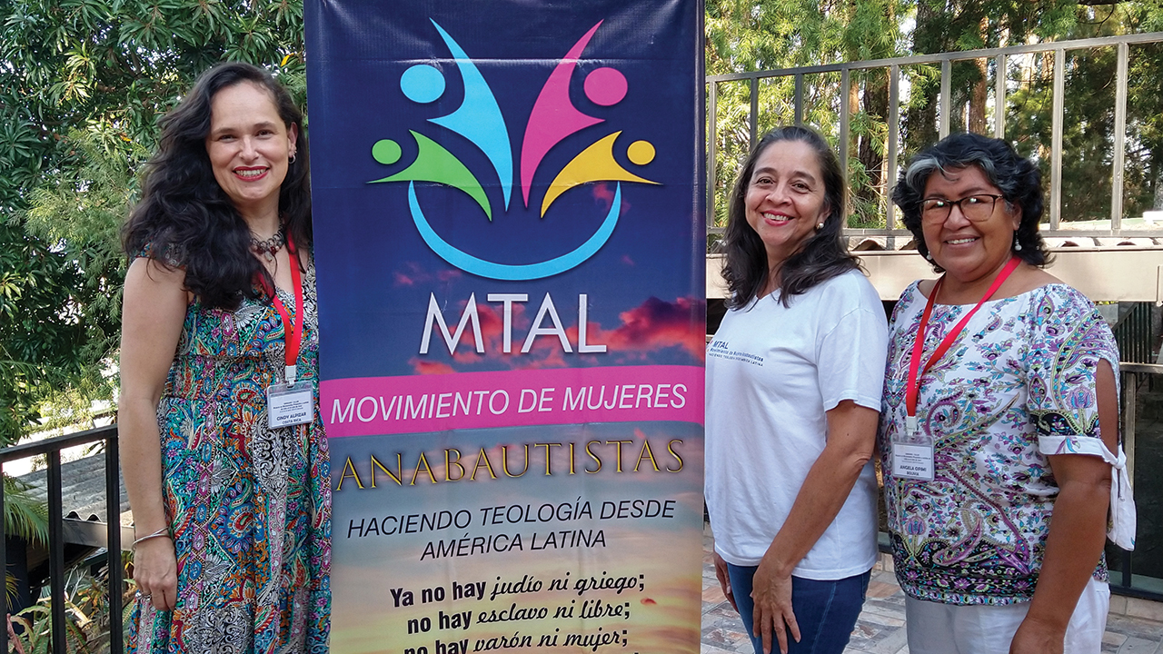 Cindy Alpízar, left, of Costa Rica, displays a banner with Mary Cano, center, of Honduras and Angela Opimí of Bolivia at the anniversary gathering of the Movement of Anabaptist Women Doing Theology from Latin America. — Linda Shelly/MMN