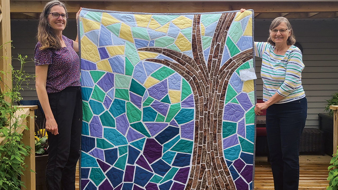 Sara Cressman, left, and Susan Cressman hold a quilt sold at the New Hamburg Mennonite Relief Sale in May. Susan Cressman won the auction of her daughter’s quilt and is donating it to Conrad Grebel University College. — David Martin