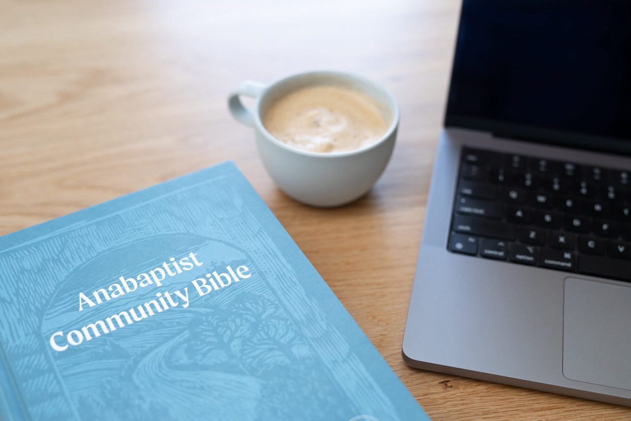 Blue Bible next to gray laptop computer and white cup of coffee