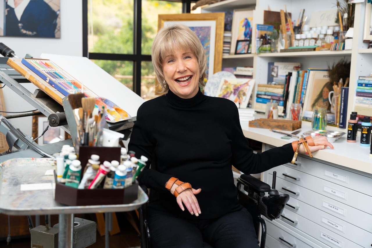 Joni Eareckson Tada sits in a wheel chair, surrounded by art supplies.