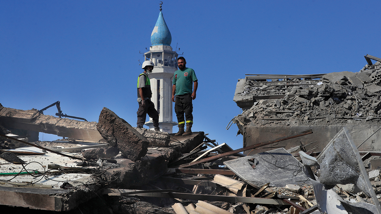 A Hezbollah rescue worker, left, and a Lebanese Civil Defence worker stand Oct. 13 on the rubble of destroyed buildings at commercial street that was hit the previous night by Israeli airstrikes, in NAbatiyeh town, south Lebanon. — Mohammed Zaatari/AP