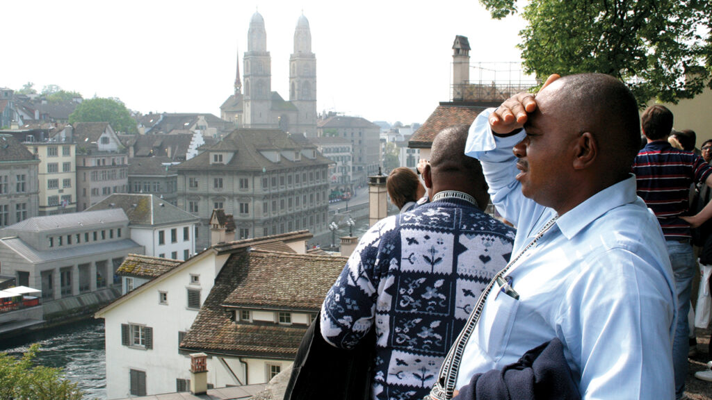 PAST INSPIRES PRESENT — Ambroise Mwanda of the Democratic Republic of Congo looks across the Limmat River in Zurich, Switzerland, where Felix Manz was drowned. “It is a big discovery to be here, to get to know my origin of Anabaptism,” Mwanda said. He was in Zurich for a meeting of the Mennonite World Conference General Council in 2012. In the distance are the twin towers of the Grossmünster church, where Ulrich Zwingli inspired Conrad Grebel and others to break from Catholicism and then from Zwingli, too. Despite fierce persecution, Anabaptism spread rapidly throughout Europe and, eventually, around the world. — Tim Huber/Mennonite World Review