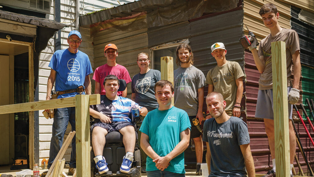Members of a high school youth group from Columbus Mennonite Church in Ohio stand with Matthew Kennedy while building a wheelchair ramp at Kennedy’s home in Kimball, W.Va., on June 4, 2024. Back row, from left: Lee Martin, Malakai Troyer, Eliza Graber, Gabriel Coble, Isaiah Turkley, Henry Wyse. Front: Matthew Kennedy, Micah Dodson, Mark Rupp. — Christy Kauffman/MCC