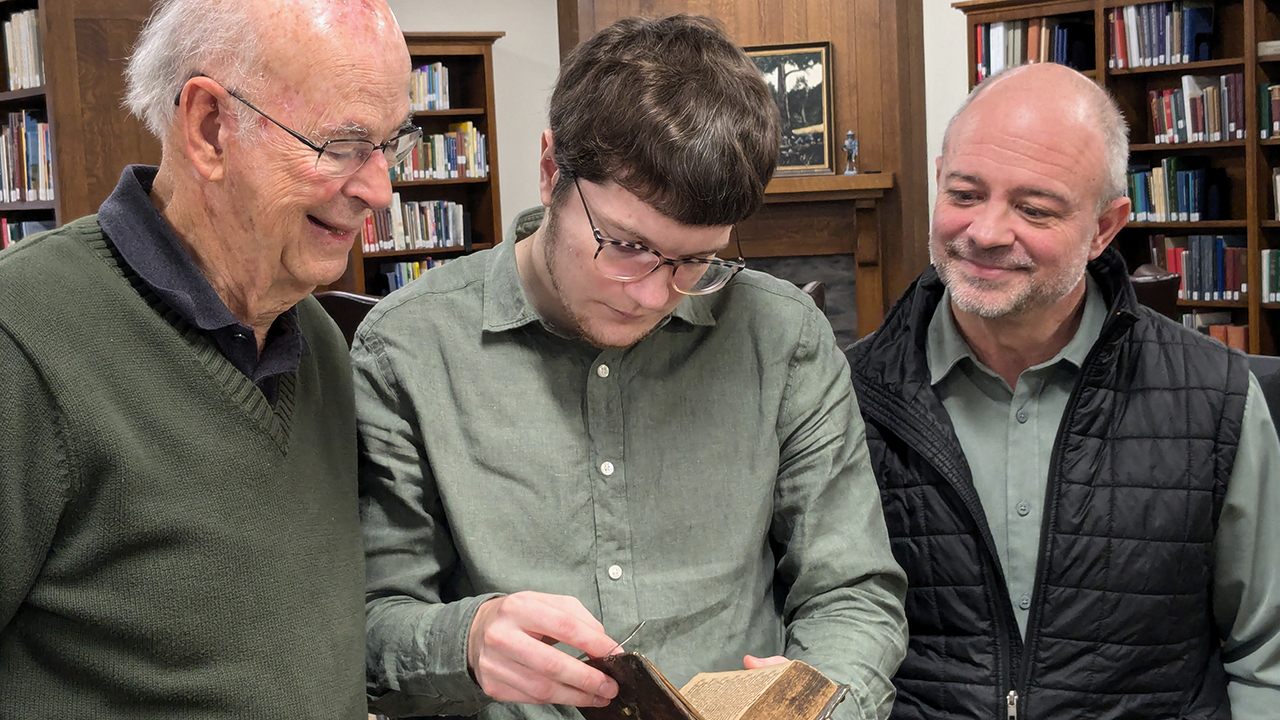 Robert Martin, left, looks over his family’s Ausbund hymnal with Amish and Mennonite Heritage Center archivist Adam Hershberger and executive director Marcus Yoder. — Nazareth Project