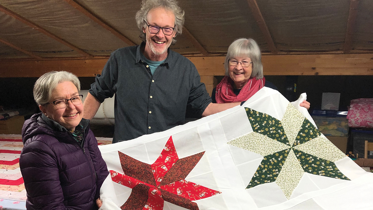 From left, Liz Driver, an MCC representative for Ukraine, and Matt Hofer and Annemarie Loose, members of the comforter group in Muttenz, Switzerland, hold a comforter made at a weekly sewing session. The Muttenz comforter group contributed their handiwork to the shipment Swiss Mennonites sent to Ukraine in the fall. — David Driver/MCC
