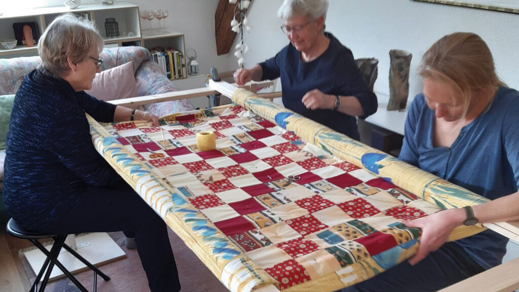 From left, Renée Braun, Anna Scherrer and Debora Stücke, participants in the Langnau comforter group, knot one of the handmade comforters which were part of a truckload of supplies from Switzerland to western Ukraine in the fall of 2024. The supplies included 400 comforters, 1,365 hygiene kits and 653 MCC relief kits. — Mennonite Central Committee
