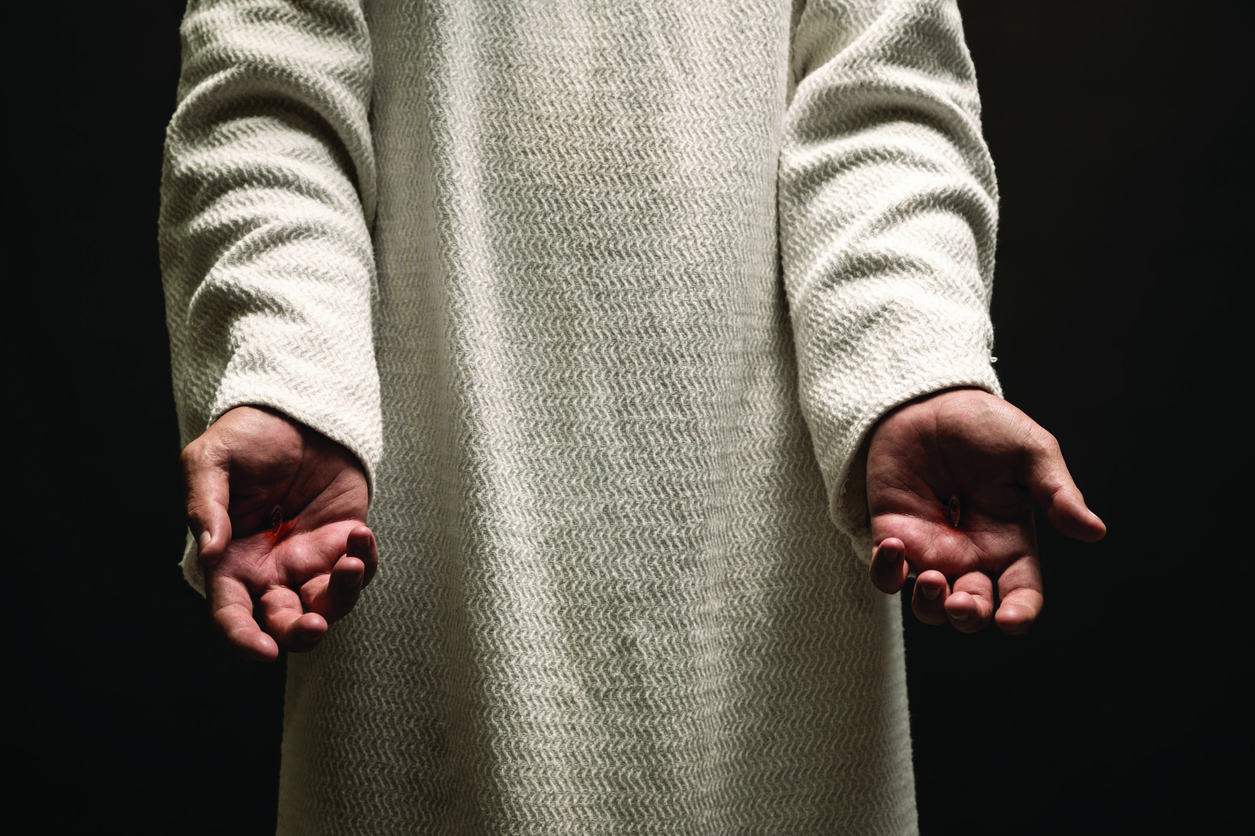 Jesus of Nazareth showing the wounds on his hands while praying on a dark night after being resurrected. Cervantes from Shutterstock.