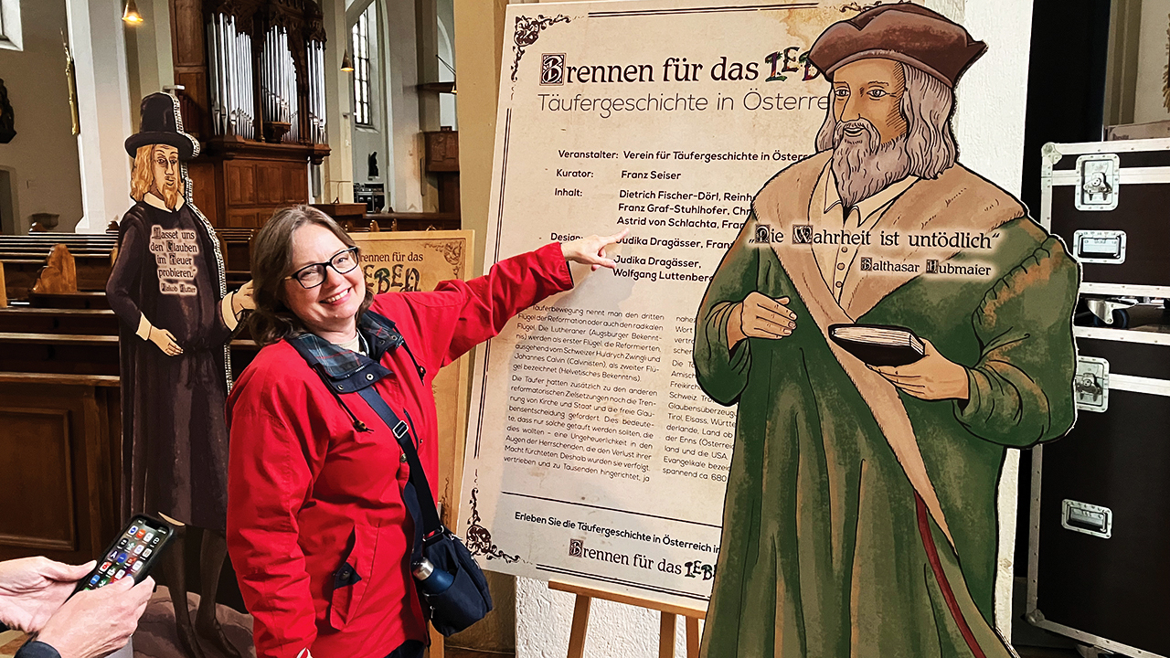 Tour co-leader Kimberly Schmidt explores an Anabaptist history display at the Kirche St. Andrä Catholic Church in Salzburg, Austria. The quote on the image of Anabaptist leader Balthasar Hubmaier says, “The truth is undying.” — Paul Schrag/AW