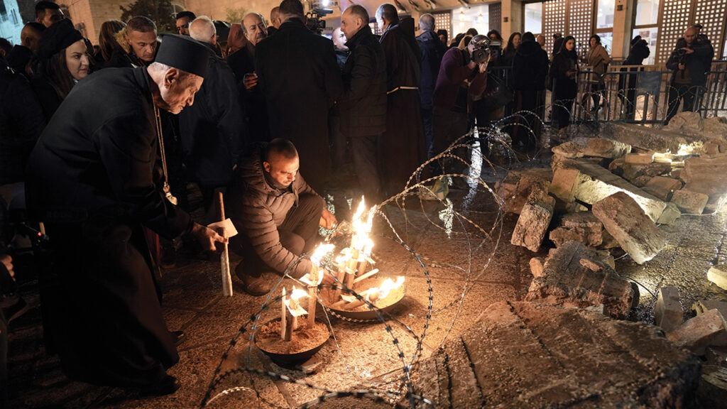 A priest and a man light candles next to a nativity scene decorated to honor the victims in Gaza and asking for peace, displayed in Manger Square, adjacent to the Church of the Nativity, in Bethlehem, on Dec. 23, 2023. — Mahmoud Illean/AP